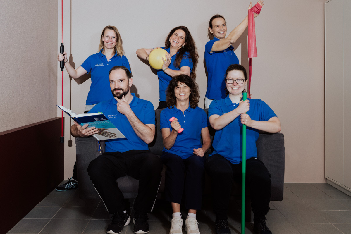 Das Team von Pro Physio in blauen Praxis-Shirts, gut gelaunt mit Therapiebändern und Ball